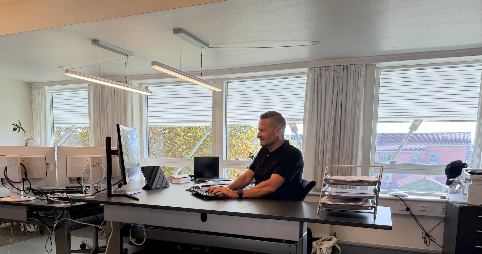 Kontorlandskab med hæve-sænkebord, buet skærm og medarbejder ved tastaturet i Tune Erhvervspark
